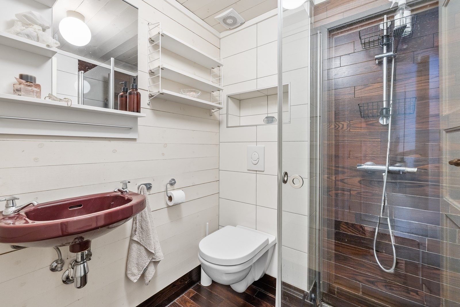 Badet er praktisk innredet med dusjhørne, vegghengt toalett, servant, speil og praktiske hyller. Galleribilde