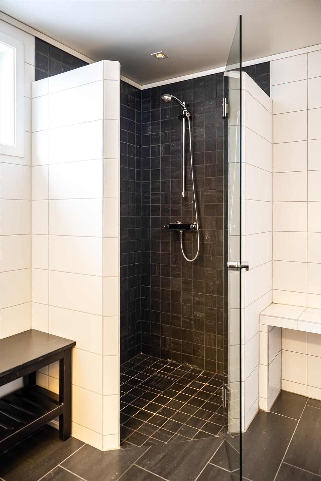 Moderne dusjnisje med mørke fliser, glassdør og minimalistisk design som gir badet et stilrent og elegant uttrykk. Galleribilde
