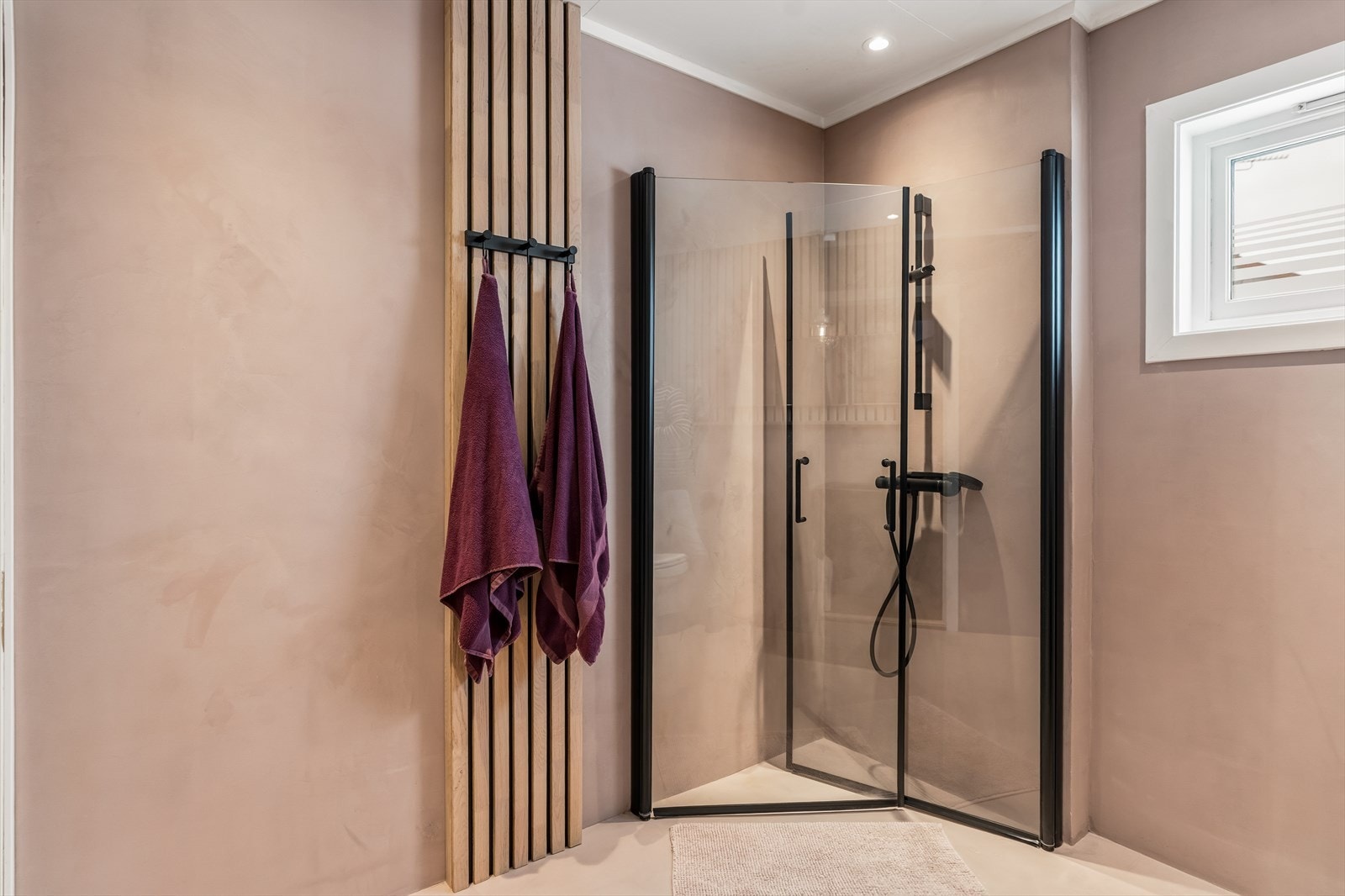 Dusjhjørnet er utstyrt med innfellbare glassdører i sort innramming. Langs den ene veggen har badet en plassbygd hylleløsning for planter, oppbevaring eller annen dekor. Galleribilde