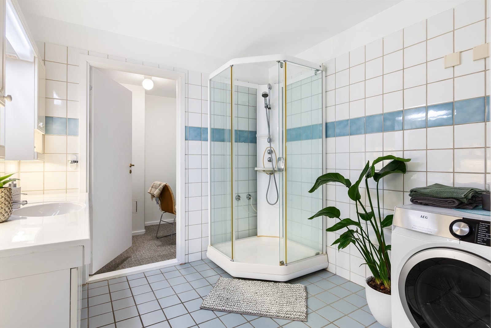 Badet er innredet med benkeplate, servantskap med nedfelt servant, speil med tilhørende sideskap og belysning over, samt dusjkabinett. Galleribilde