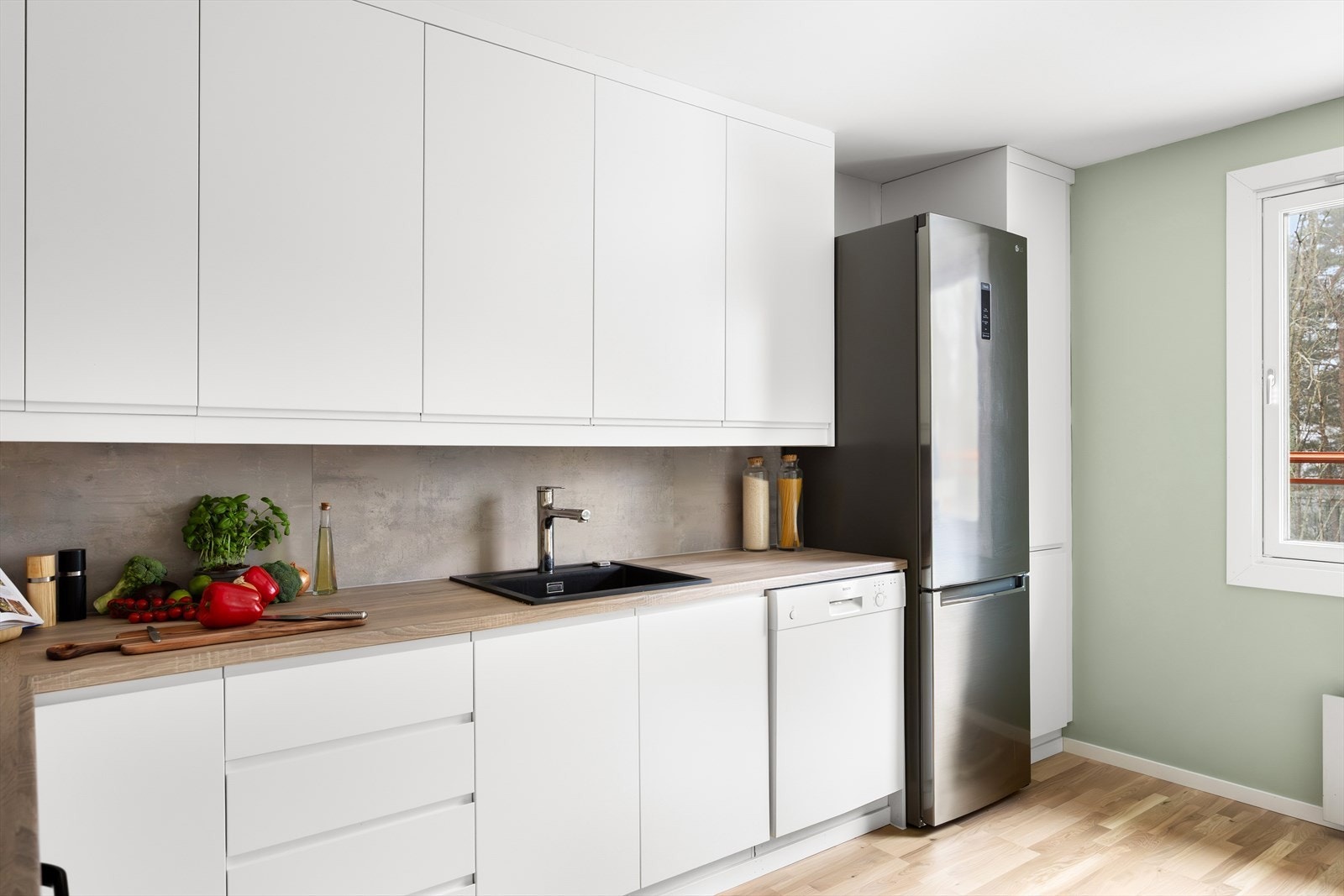 Kjøkkeninnredningen har hvite, glatte fronter og laminat benkeplate med nedfelt oppvaskkum og ettgreps svingbart blandingsbatteri. Galleribilde