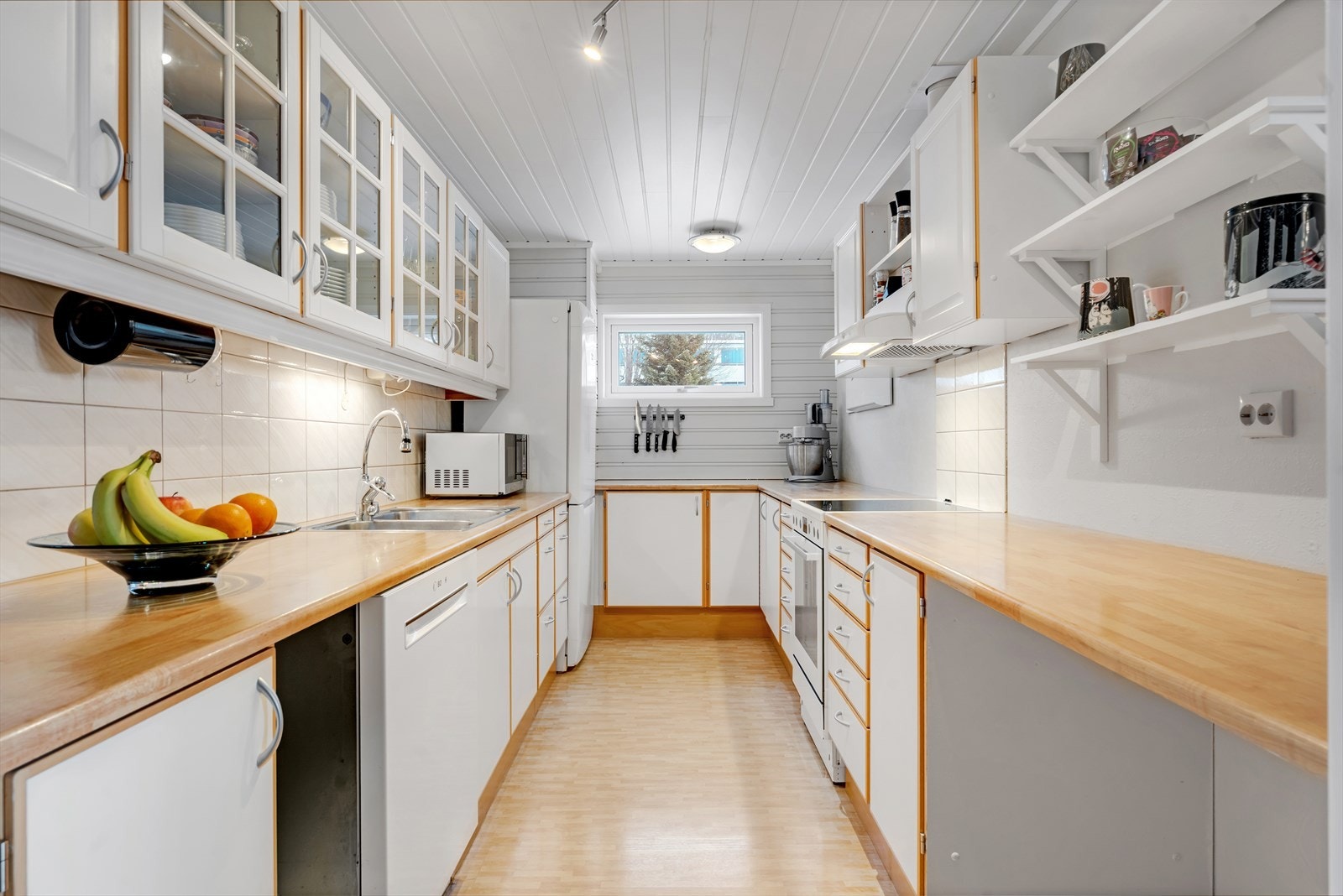 Flott kjøkken i hvit utførelse med rikelig oppbevaringsplass i hyller og skap. Galleribilde