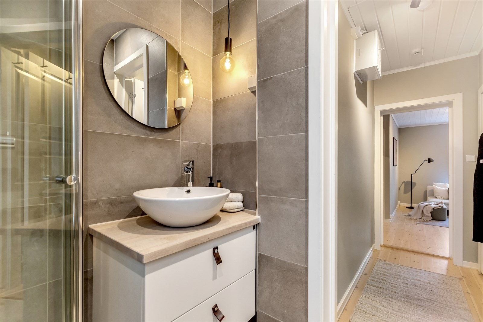 Badet er innredet med dusjhjørne med glassdører og servant med underskap som gir praktisk oppbevaring. Galleribilde