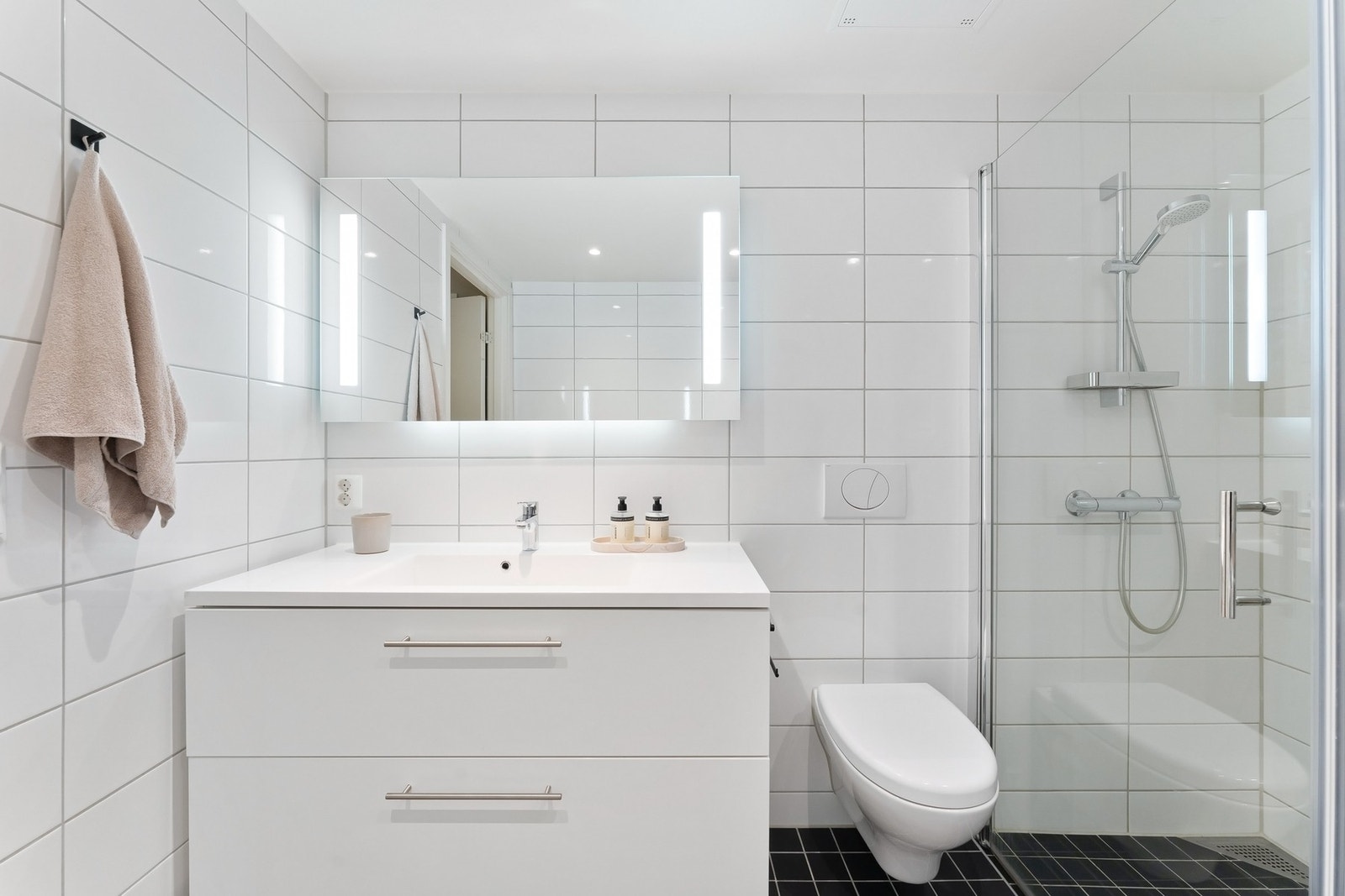 Baderommet er innredet med vegghengt toalett, dusjhjørne med glassdører av herdet glass og servantinnredning med speil og belysning. Galleribilde