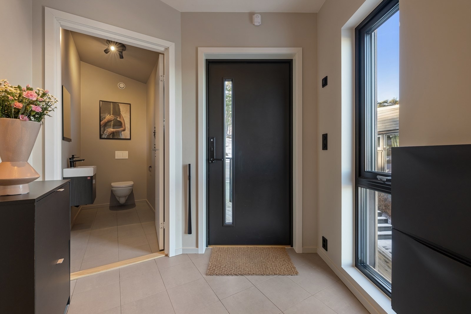 Stor og romslig entré med fliser på gulv og behagelig gulvvarme. Det er også et toalettrom med nedfelt servant og vegghengt toalett. Galleribilde