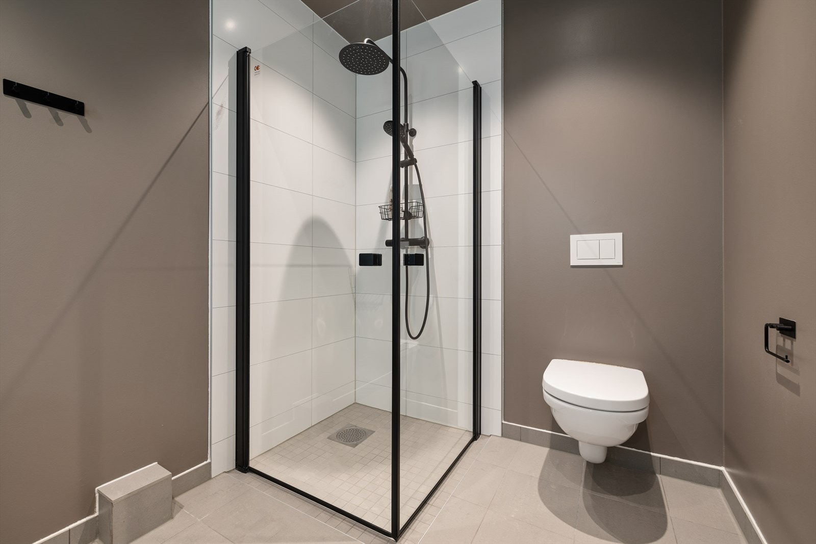 Flislagt dusjhjørne med innfellbare glassdører, dusjarmatur med regnfallsdusj og vegghengt toalett. Galleribilde