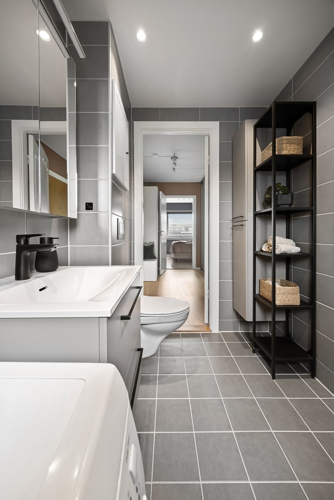 Stilrent bad som er innredet med servant m/skuffer, vegghengt speil m/belysning, veggmontert toalett og dusjhjørne med innfellbare dører. Galleribilde