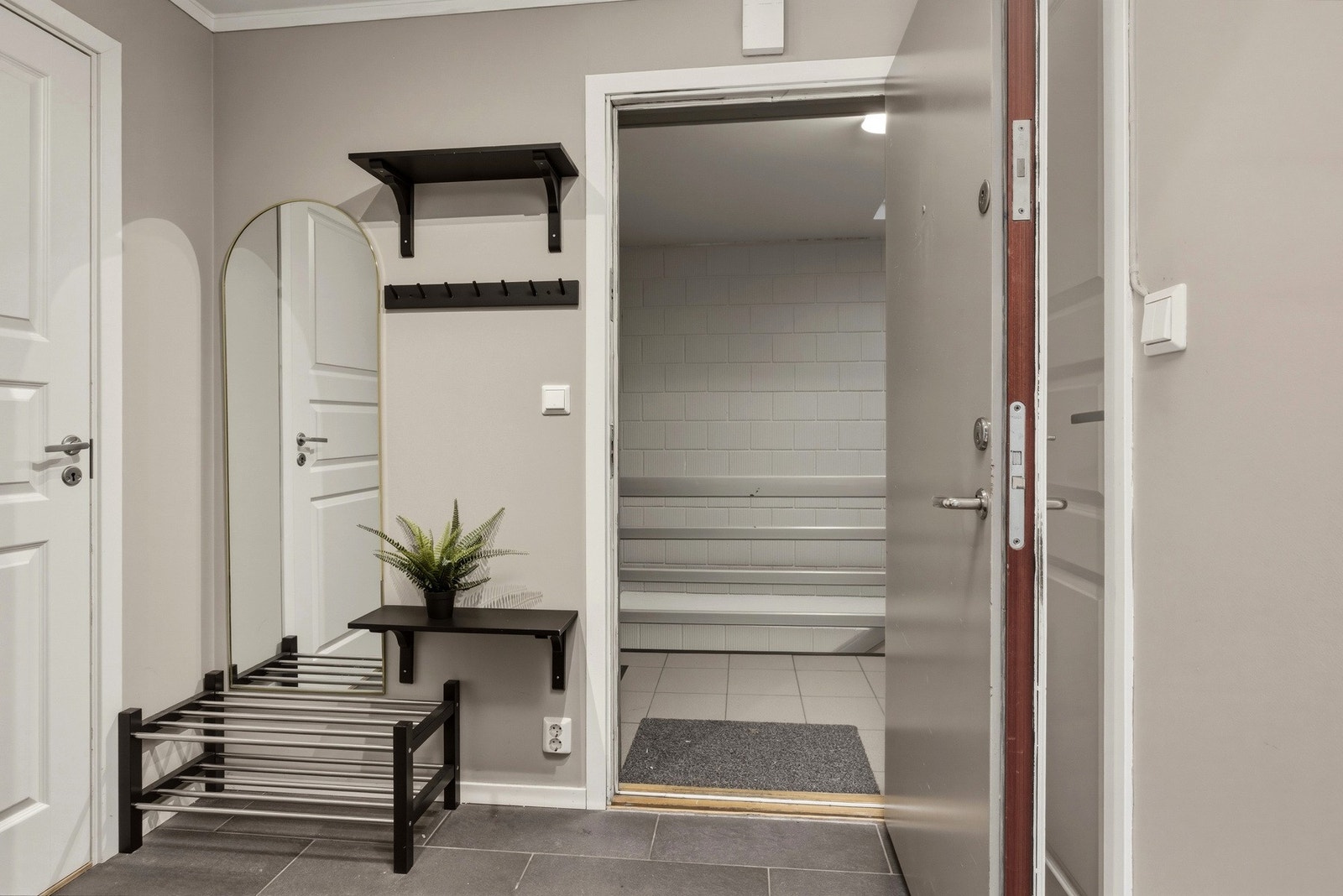 Entreen har fliser på gulv, glatte, beige veggflater, samt noen hyller og knagger. Leiligheten ble pusset opp i 2021. Galleribilde