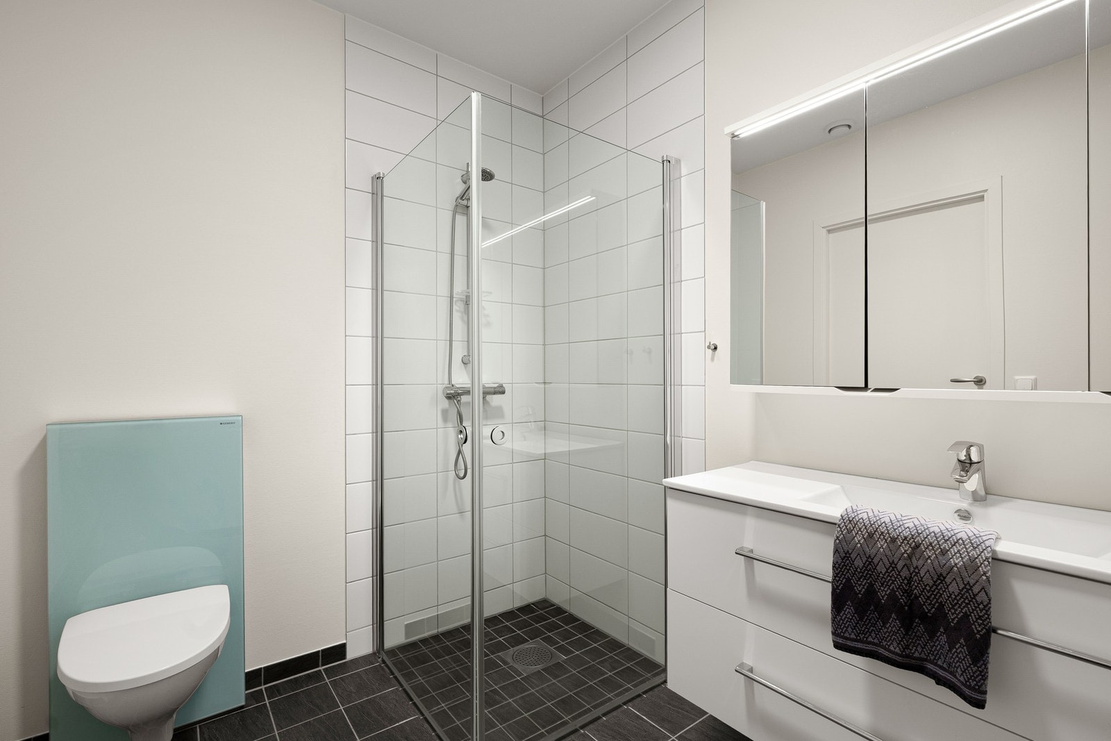 Badet fremstår som moderne og delikat, med hvite fliser og hvitmalte overflater på veggene og med koksgrå fliser på gulv med vannbåren gulvvarme. Galleribilde