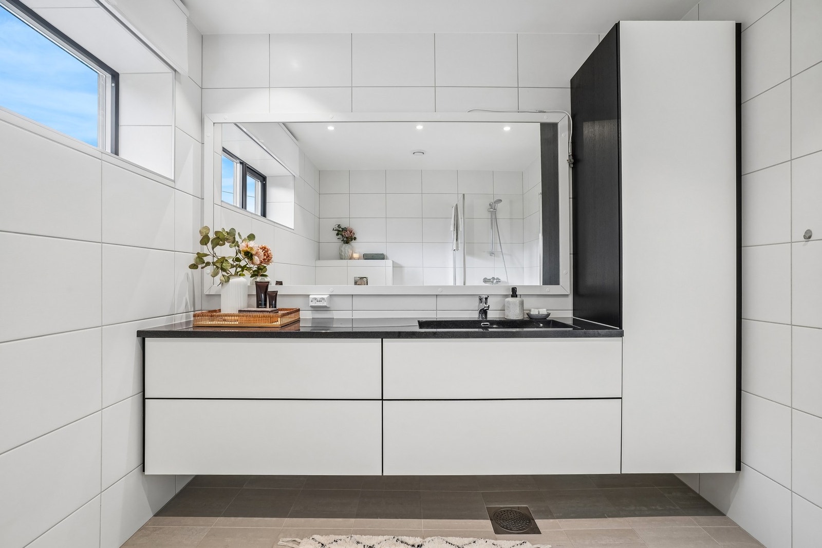 - og en stor servantinnredning med hvite glatte fronter, helstøpt kompositt servantplate, stort speil med hvit omramming og et høyskap. Galleribilde