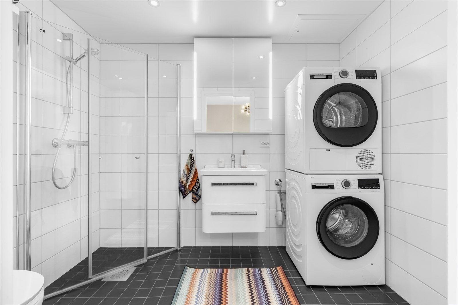 Bad 1: Badet inneholder vegghengt wc, dusjhørne med glassdører, servant med skuffer, speilskap med lys og opplegg for vaskemaskin og tørketrommel. Galleribilde