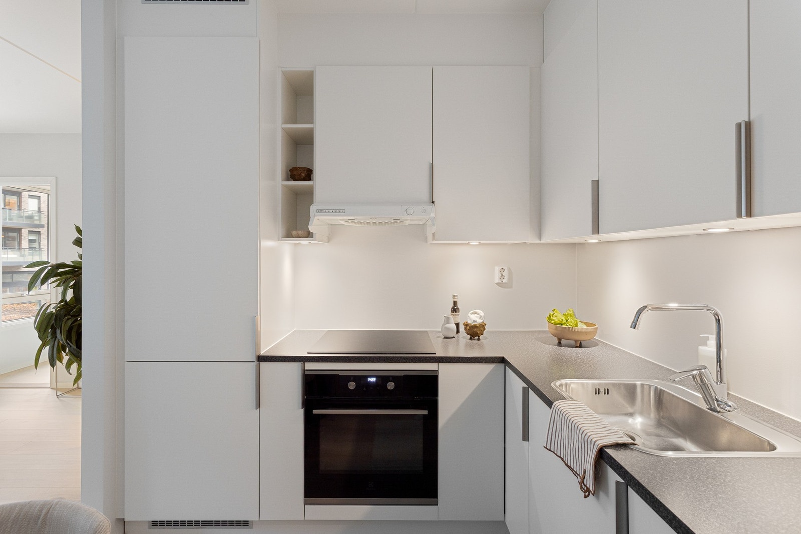 Lys, glatt innredning med laminat benkeplate og kum i rustfritt stål med ett-greps armatur. Galleribilde