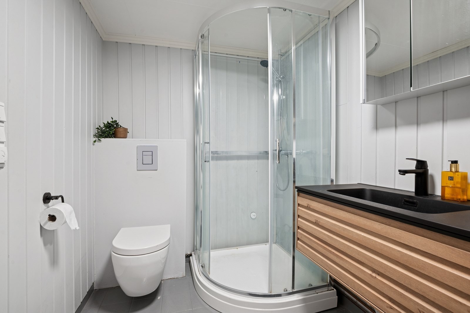 Baderom innredet med servant med underskap, speilskap, dusjkabinett og vegghengt toalett. Galleribilde