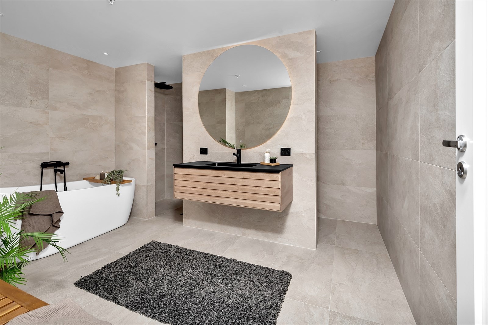 Et meget pent baderom med store fliser på vegger og gulv, badekar, dusjhjørne og skjult toalett bak vegg. Galleribilde