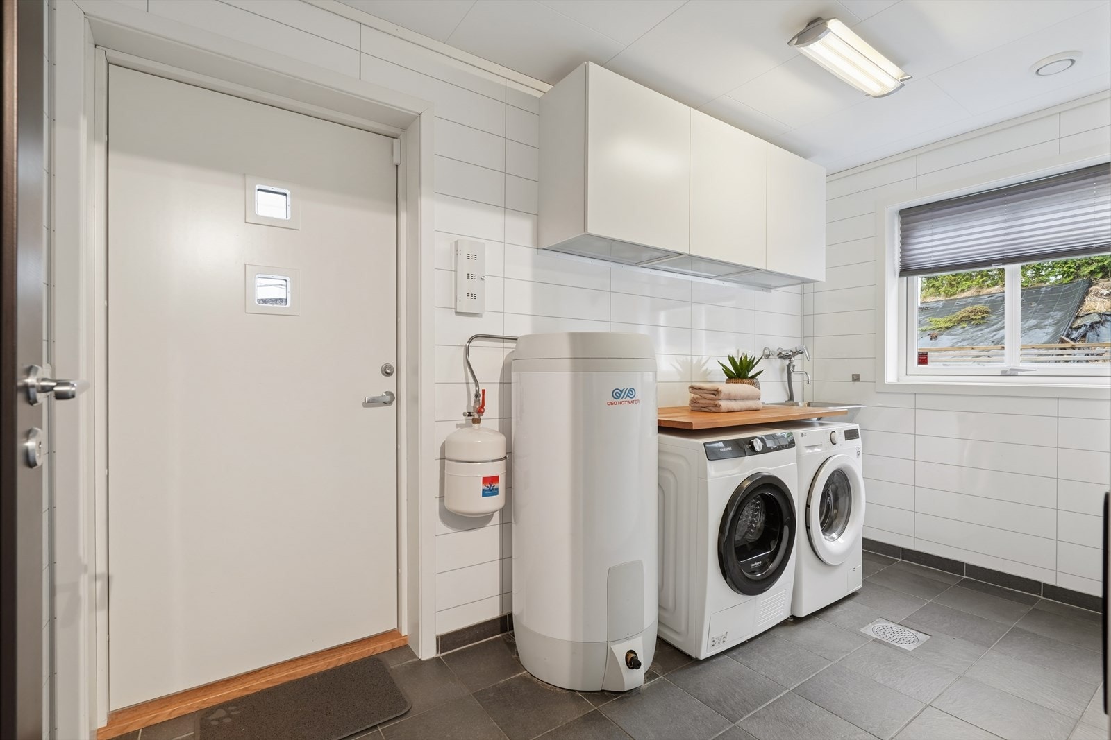 Praktisk vaskerom med flislagt gulv, egen utgang og opplegg for vaskemaskin og tørketrommel. Galleribilde