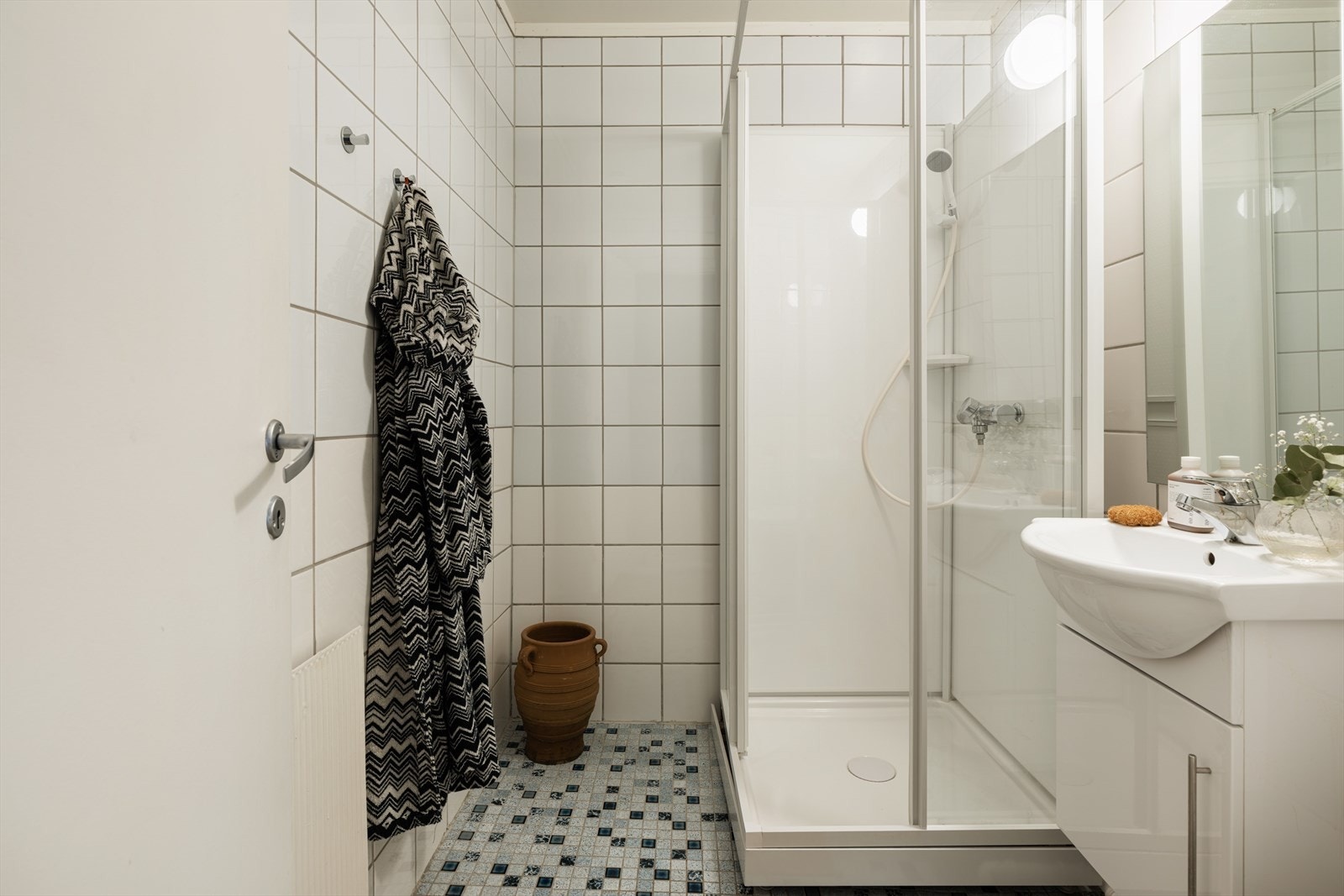 Flislagt bad med dusjkabinett, vegghengt servant med underskap, vegghengt speil med overlys og gulvstående toalett. Galleribilde