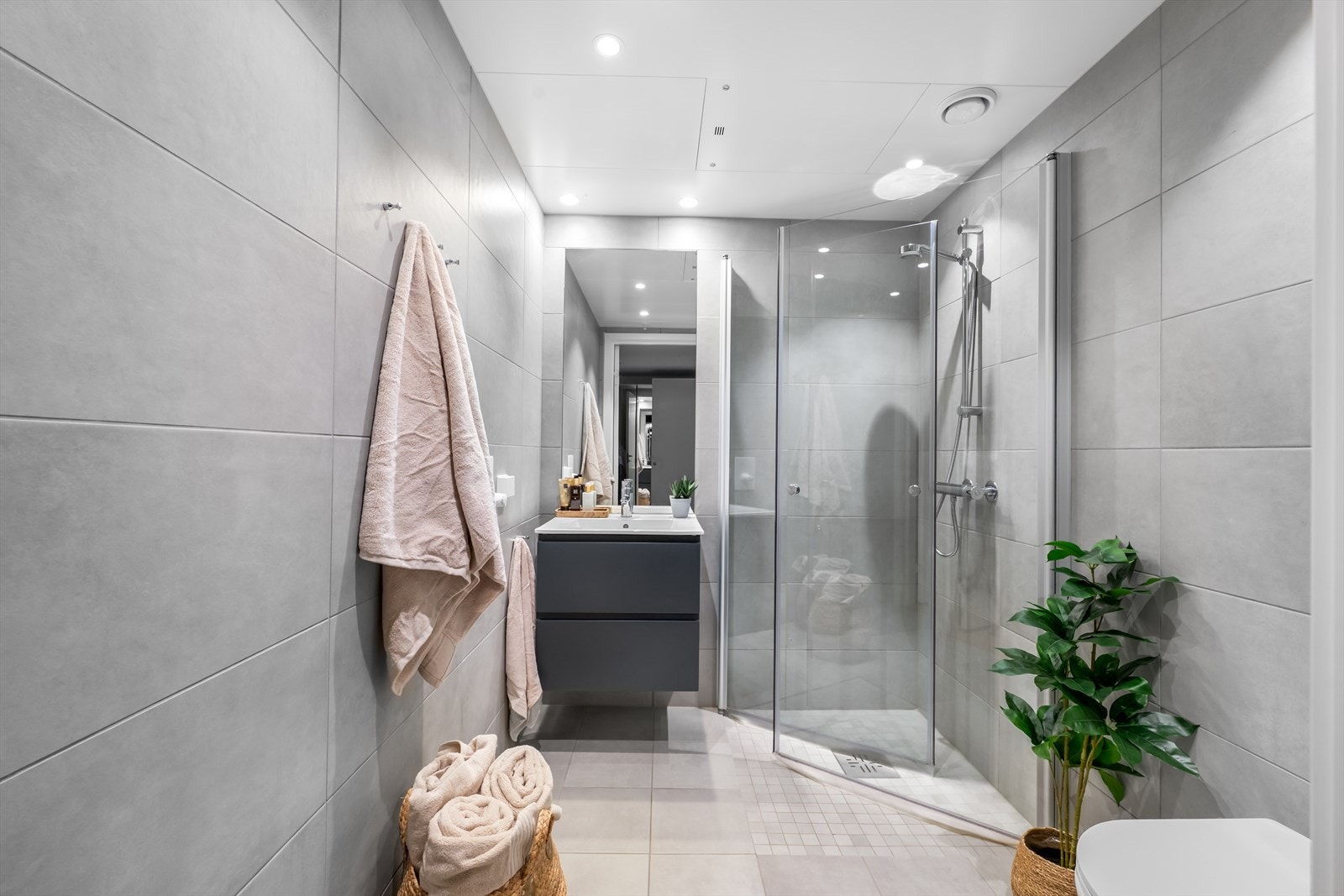 Flislagt bad på ca. 3,9 m² med vannbåren gulvvarme, vegghengt toalett og dusjhjørne med innsvingbare glassdører. Galleribilde