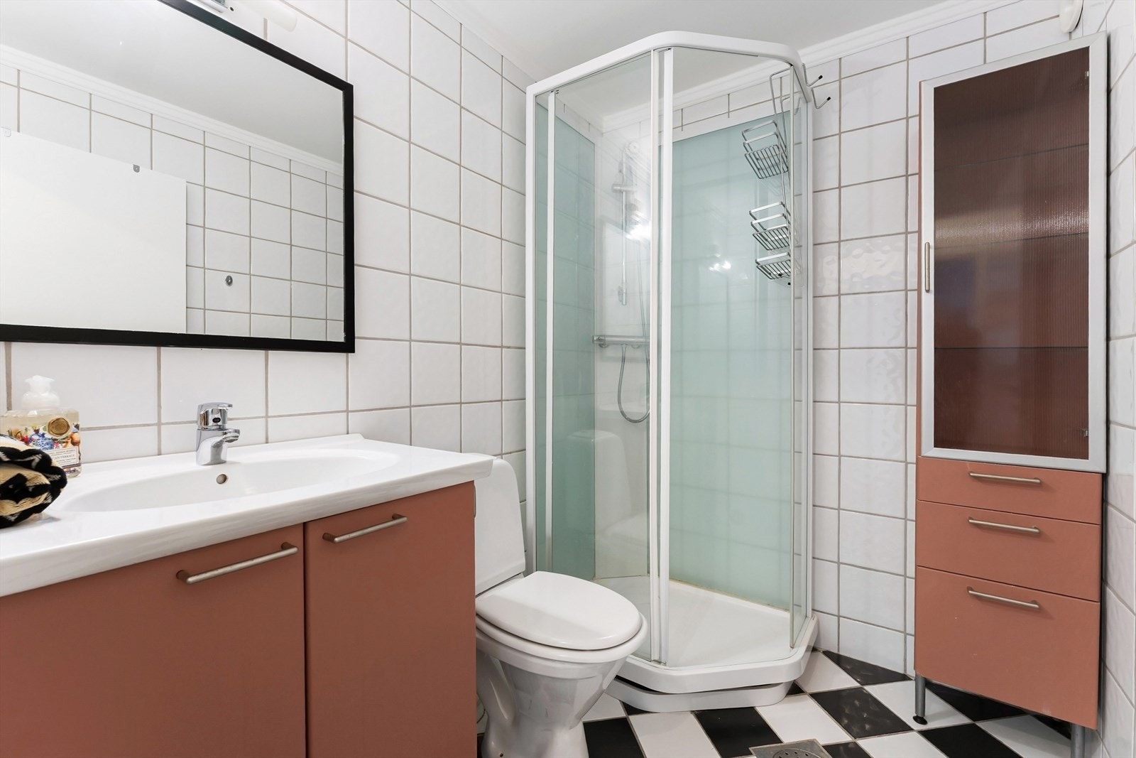 Flislagt baderom utstyrt med wc, servant med innredning, speil og dusjkabinett Galleribilde