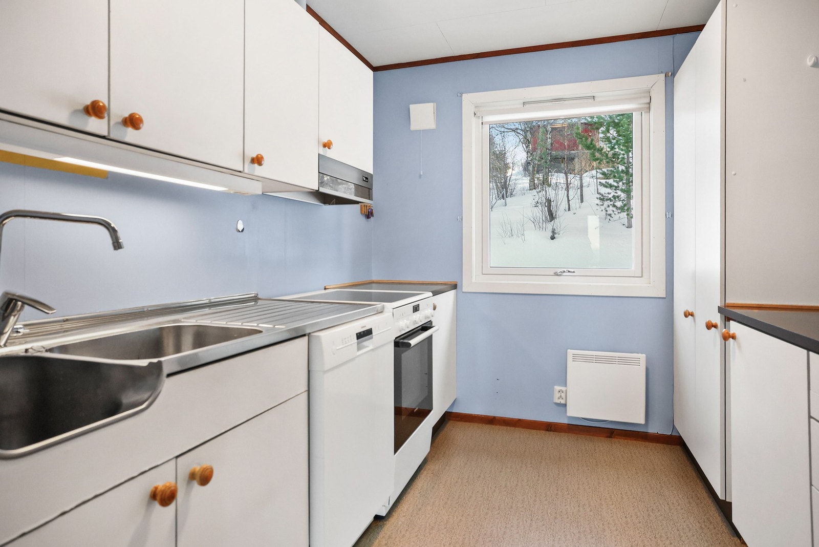 Kjøkkeninnredningen har glatte fronter og benkeplate av laminat og rustfritt stål med nedfelt oppvaskkum. Galleribilde