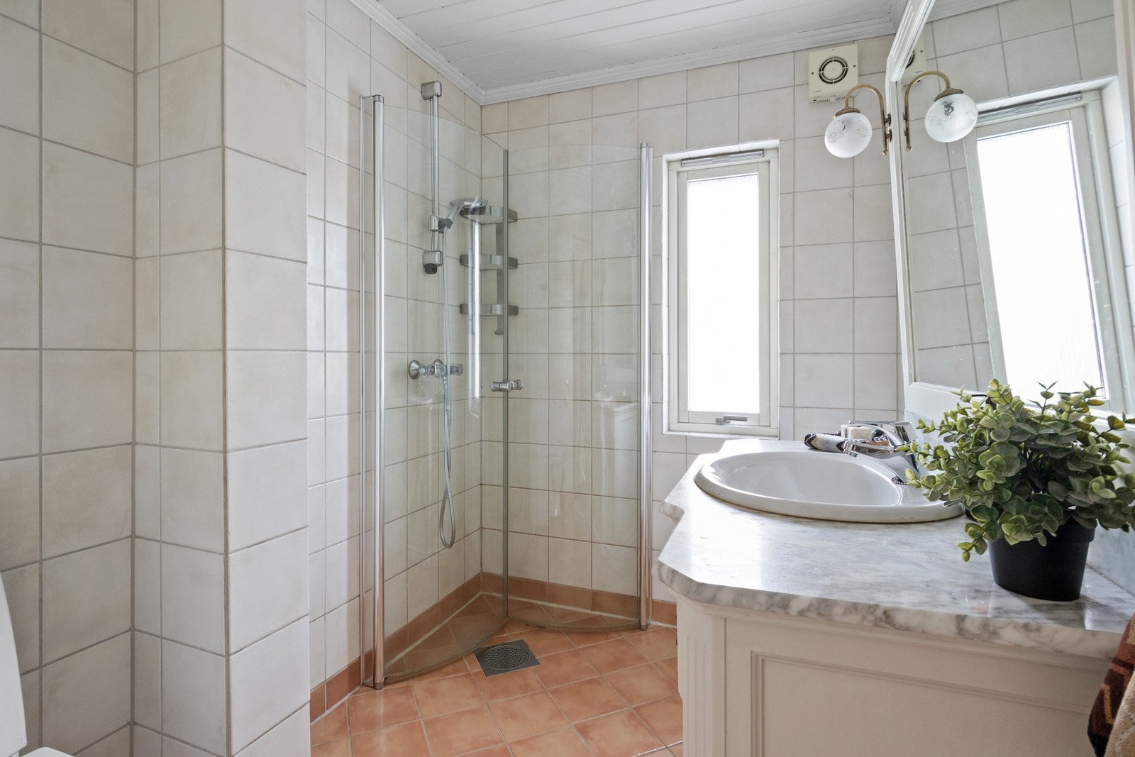 Badet fremstår som velholdt og pent, med lyse fliser på veggene og terracottafargede fliser på gulv med gulvvarme. Galleribilde