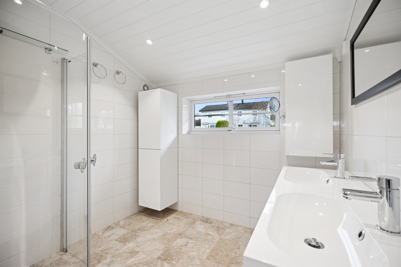 Delikat, flislagt bad med gulvvarme, baderomsinnredning med to servanter og veggskap med glatte fronter i høyglanset utførelse. Galleribilde