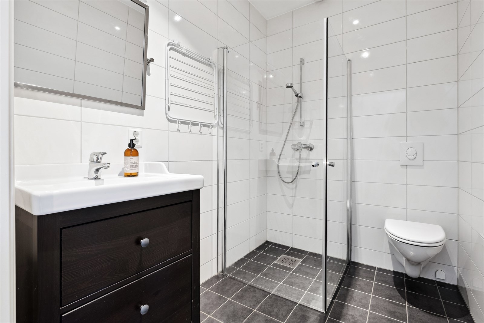 Flislagt bad i 1. etasjen er utstyrt med gulvvarme, vegghengt toalett, dusjhjørne med glassdører og baderomsinnredning med servant. Galleribilde