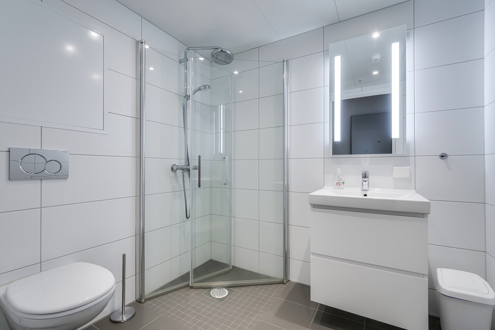 Pent bad med klosett, dusjhjørne og servant med innredning. Galleribilde