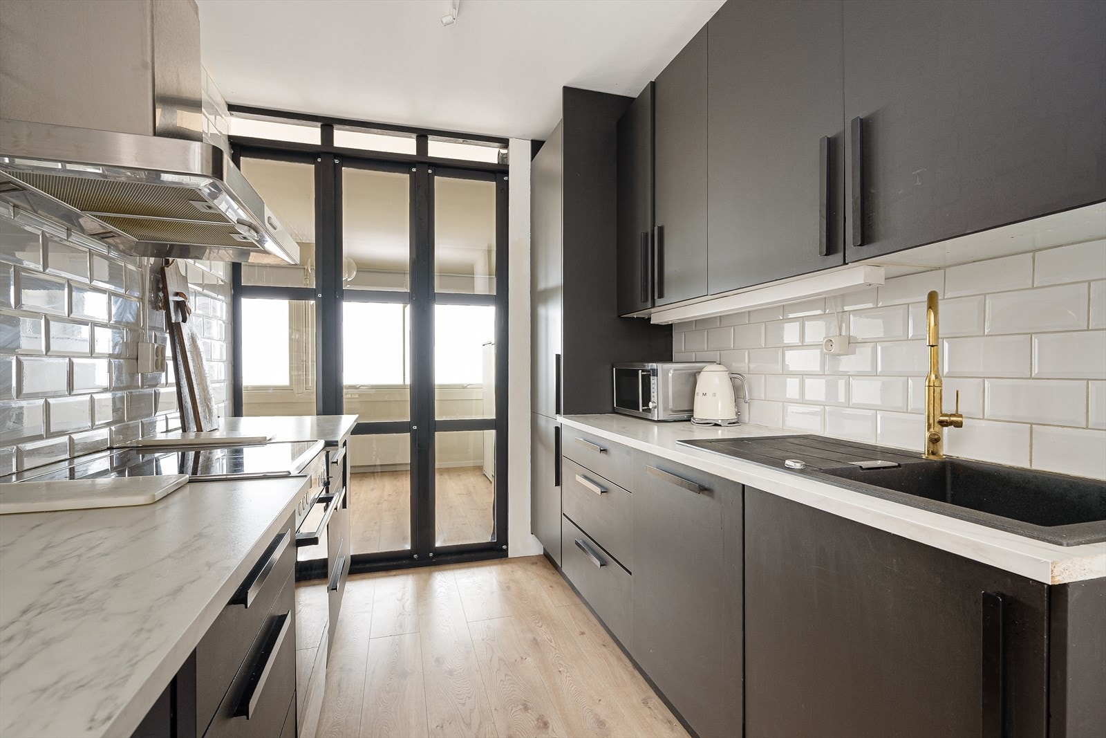 Kjøkkenet har innredning med slette fronter og benkeplate med oppvaskkum i sort kompositt, med dekorativ flis over benk. Galleribilde