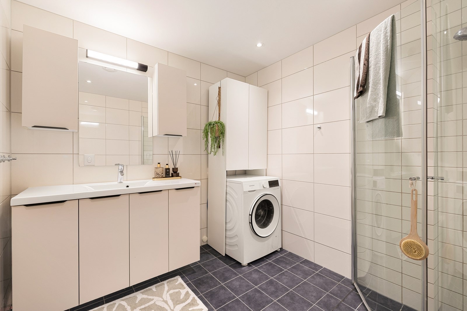 Lyst baderom med stor servantinnredning, dusjhjørne med innfellbare dører, toalett og opplegg for vaskemaskin. Galleribilde