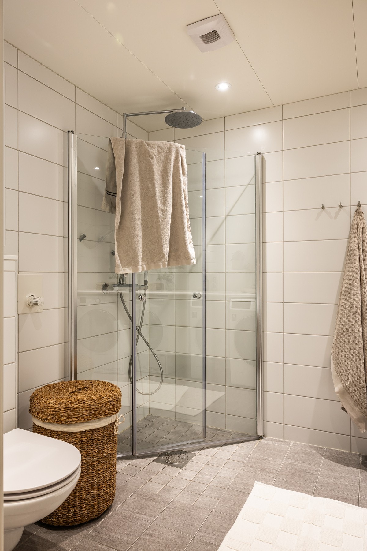 Innredet med dusj med innfellbare dusjdører, veggmontert klosett, servant på benkeplate, baderomsinnredning og opplegg for vaskemaskin. Galleribilde