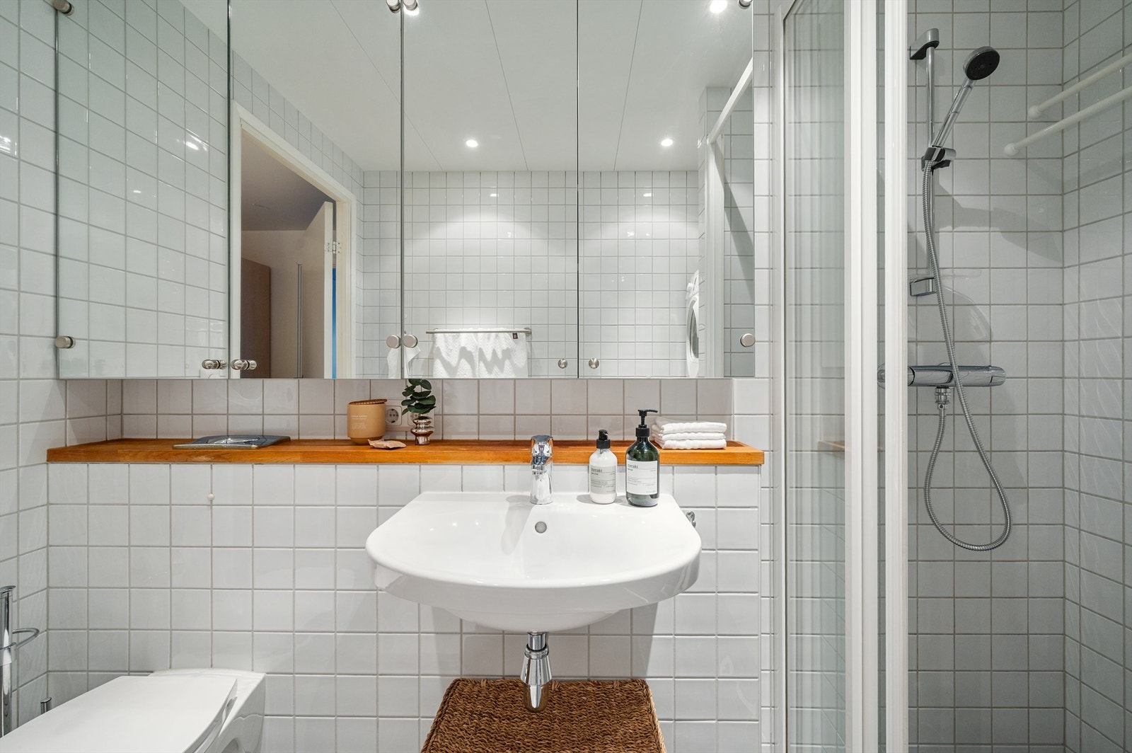 Rommet er innredet med vegghengt klosett, servant, speilskap og et dusjhjørne med skyvedør. Galleribilde