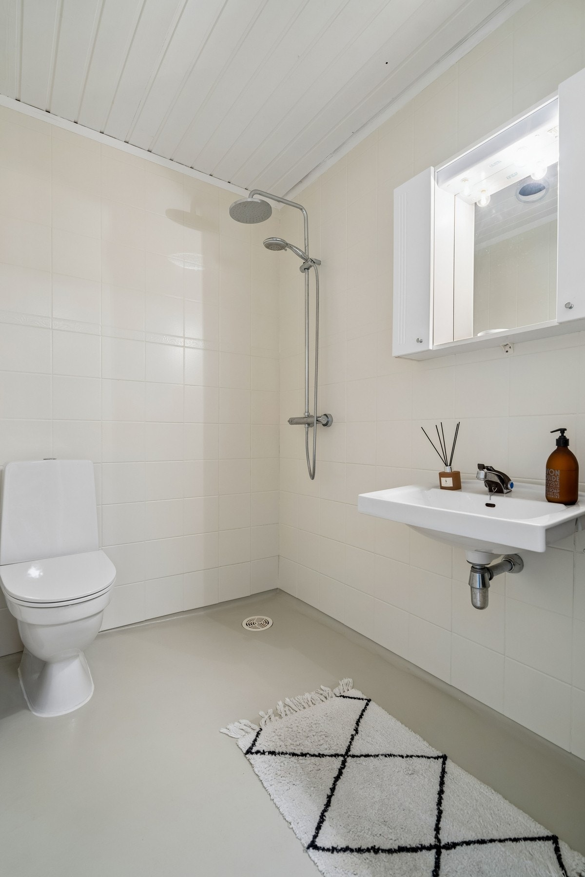 Badet har gulvstående toalett, servant på veggen og dusjhjørne. Galleribilde