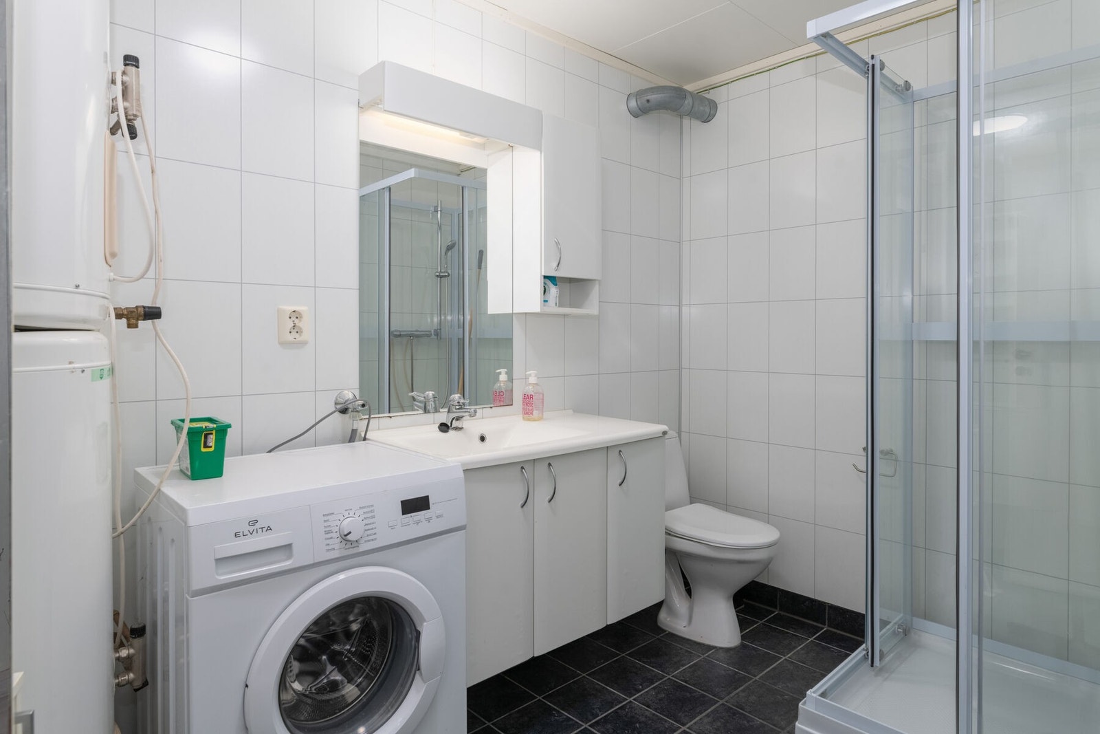 Bad 1 i underetasjen har flislagt gulv med varmekabler, og er innredet med servant, toalett, dusjkabinett og opplegg for vaskemaskin. 2 stk varmtvannstanker på 200 liter. Galleribilde