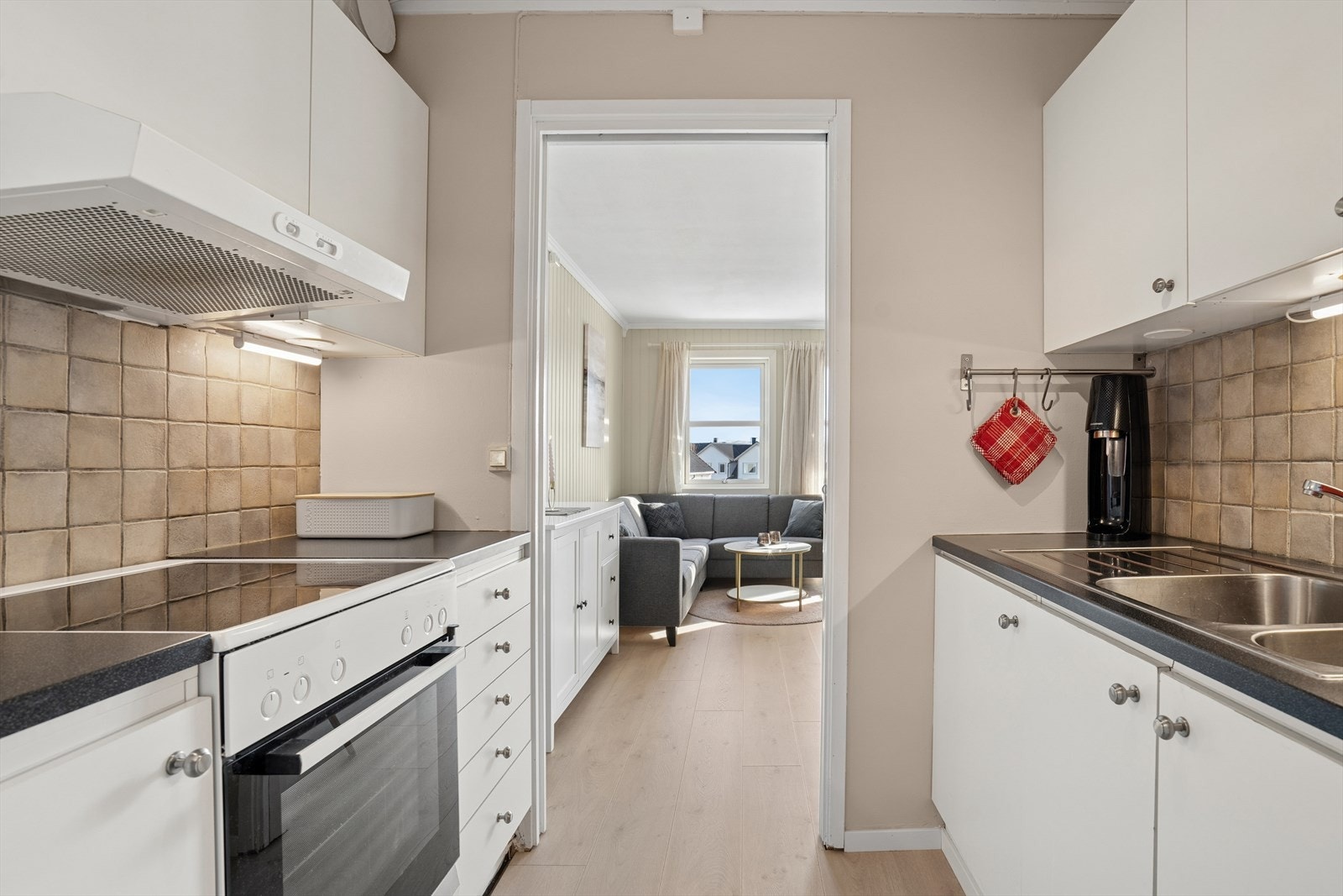 Kjøkkenet har en tidløs innredning med lyste glatte fronter, laminert benkeplate med nedfelt stålvask og fliser på vegg over benk Galleribilde