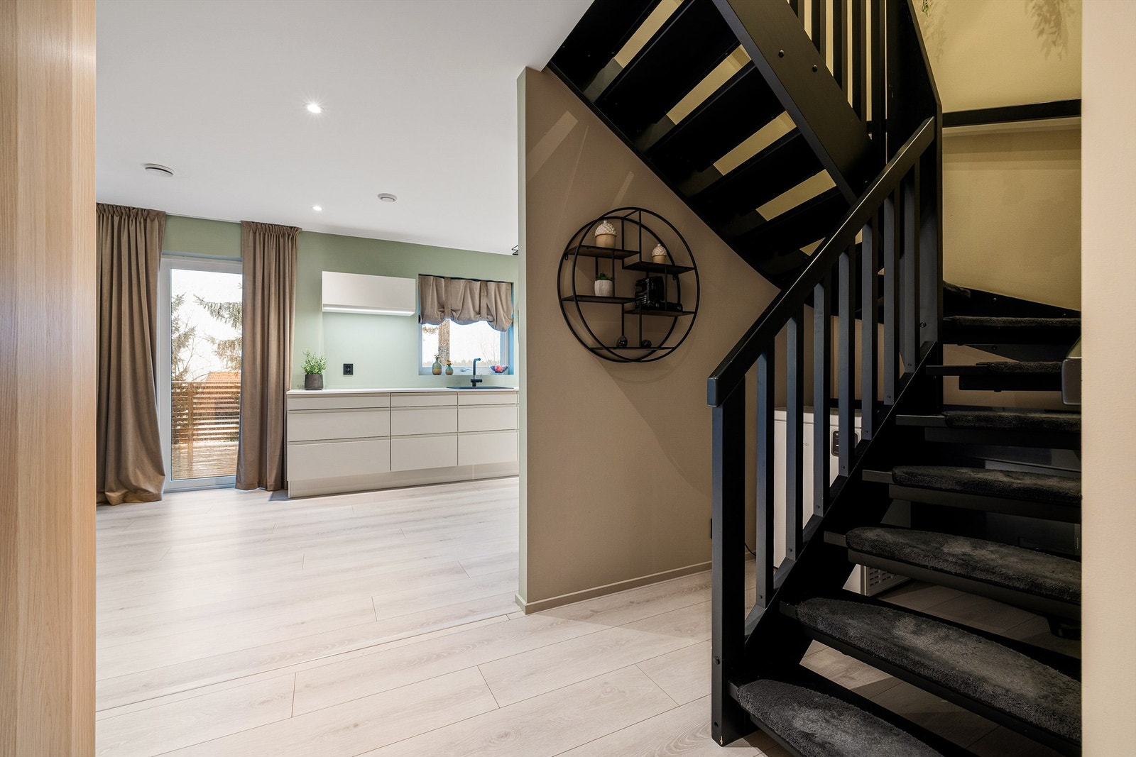 Entréen åpner inn mot kjøkken og uteplass, med skulpturell sort trapp som gir karakter og en luftig, sammenhengende planløsning. Galleribilde