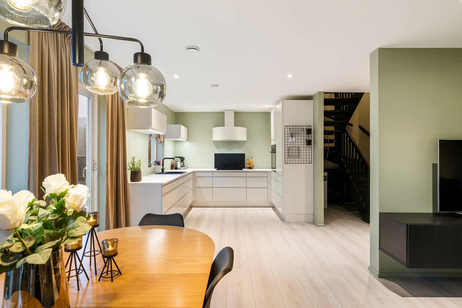 Åpent kjøkken med lyse overflater og grønn bakvegg som gir rommet en luftig, moderne følelse og fin flyt mot spisestuen. Galleribilde