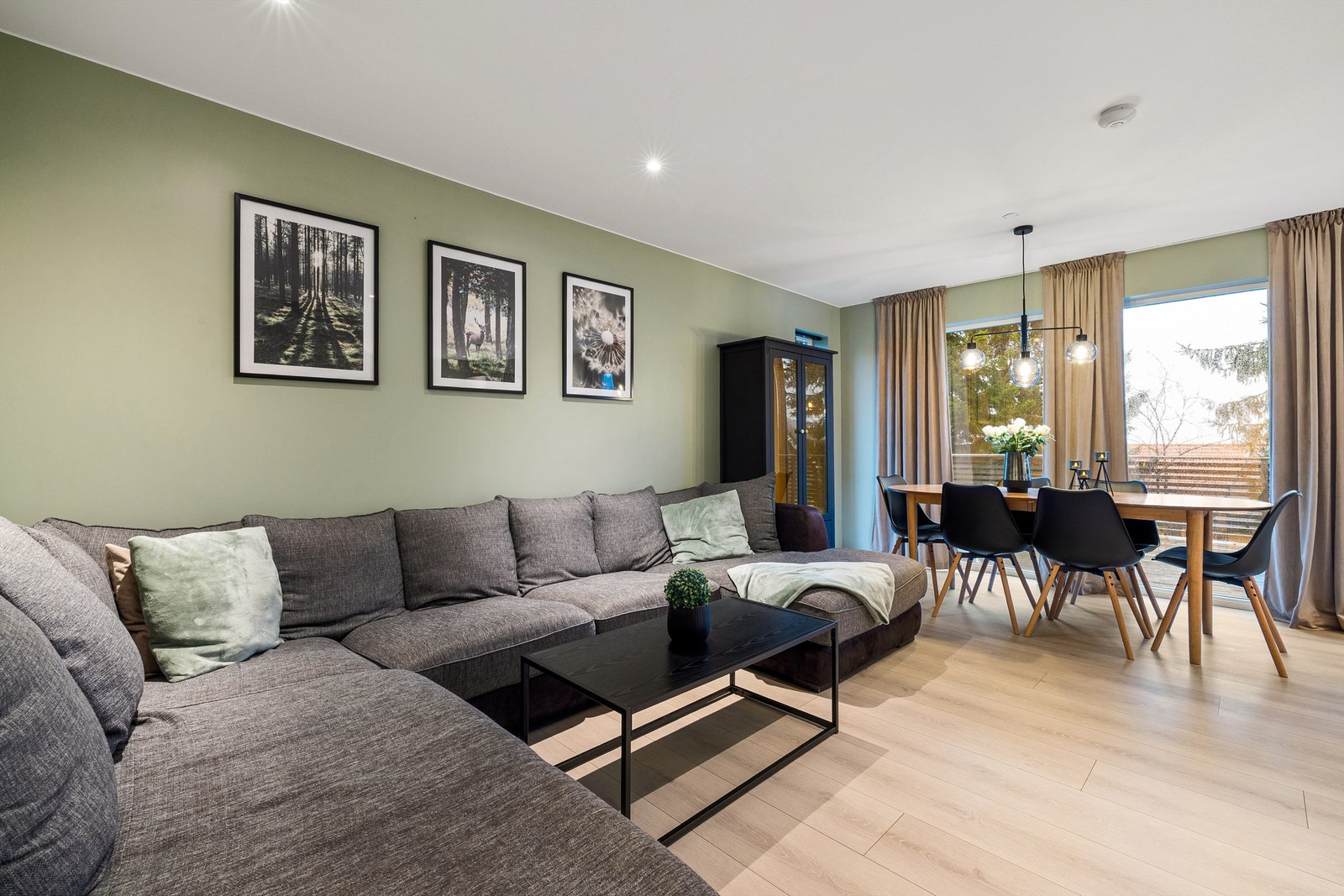 Stue med lyst gulv, varm fargepalett og utsyn mot tretoppene som gir en rolig, luftig romfølelse. Galleribilde