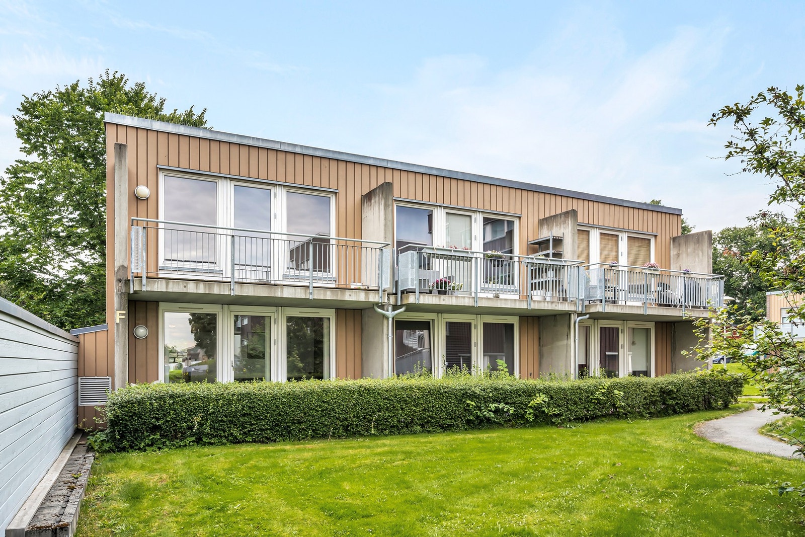 Bilde av fasaden fra sommerhalvåret. Bygget har en flott plen i forkant av balkongene/tarrassene. Galleribilde