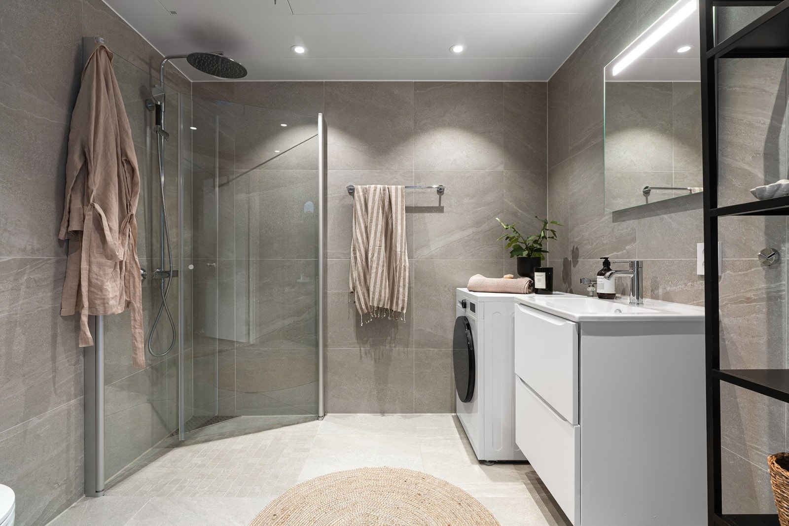 Nydelig flislagt bad - utstyrt med stort dusjhjørne, opplegg for vaskemaskin, praktisk vegghengt toalett, samt innredning med oppbevaringsplass. Galleribilde