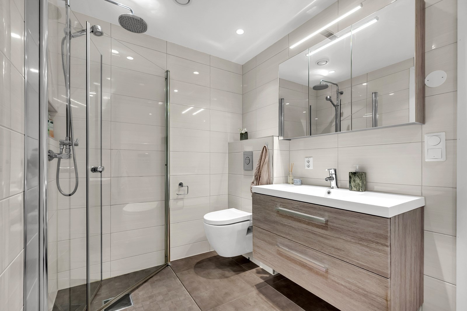 Pent flislagt bad med dusjhjørne, toalett, servant med oppbevaring og badekar. Galleribilde