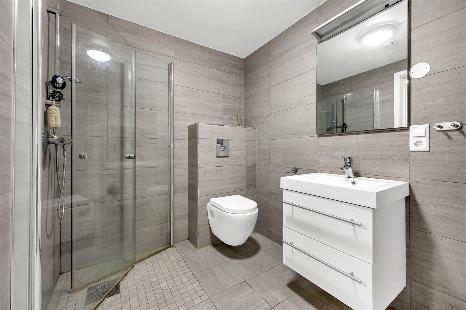 Bad med dusjhjørne, toalett og servant med innredning. Det er montert vaskemaskin i boden som ligger vegg i vegg med badet. Galleribilde