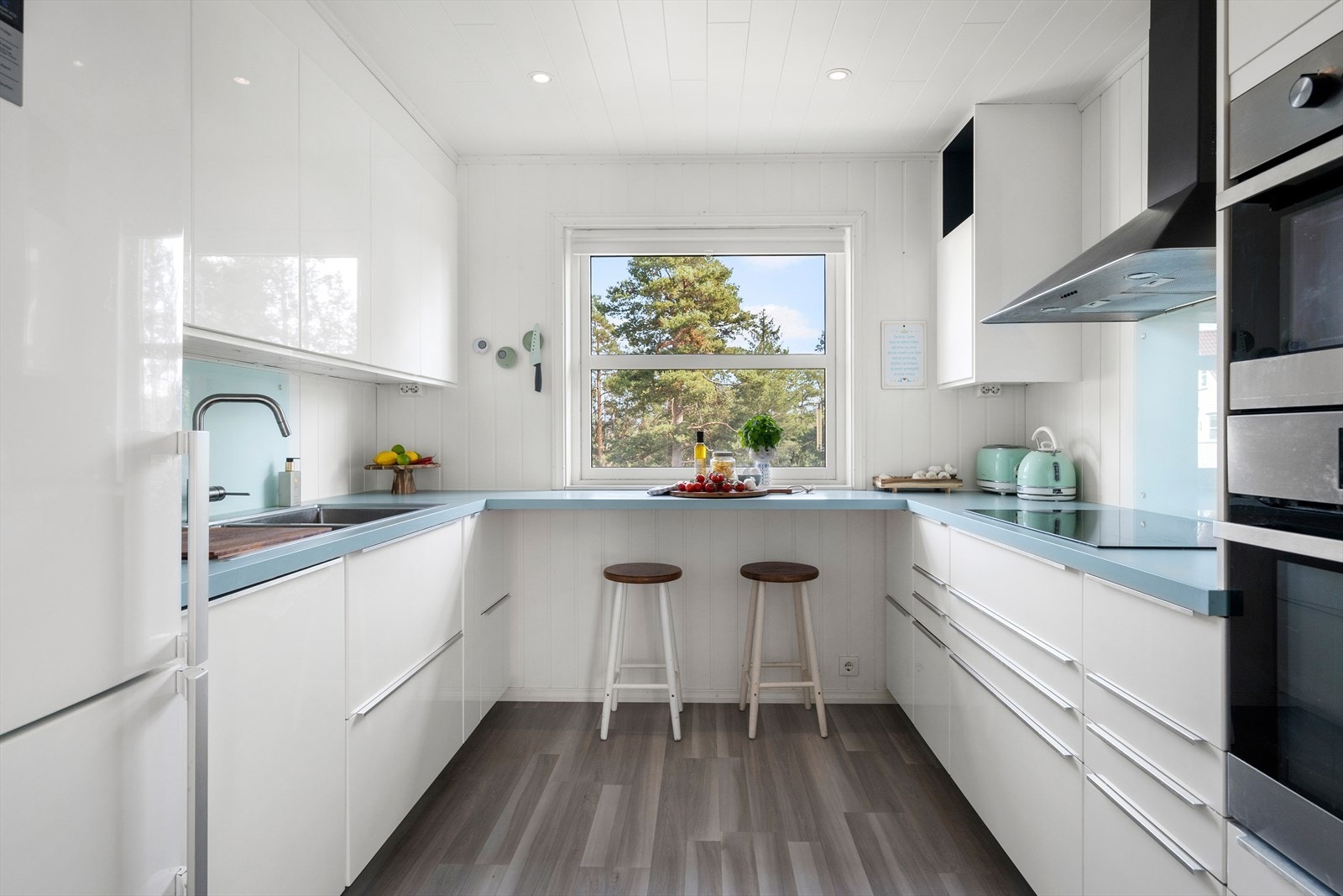 Et praktisk utformet kjøkken med innredning langs tre vegger og plass til stoler ved vinduet. Varmefolie i gulvet. Galleribilde