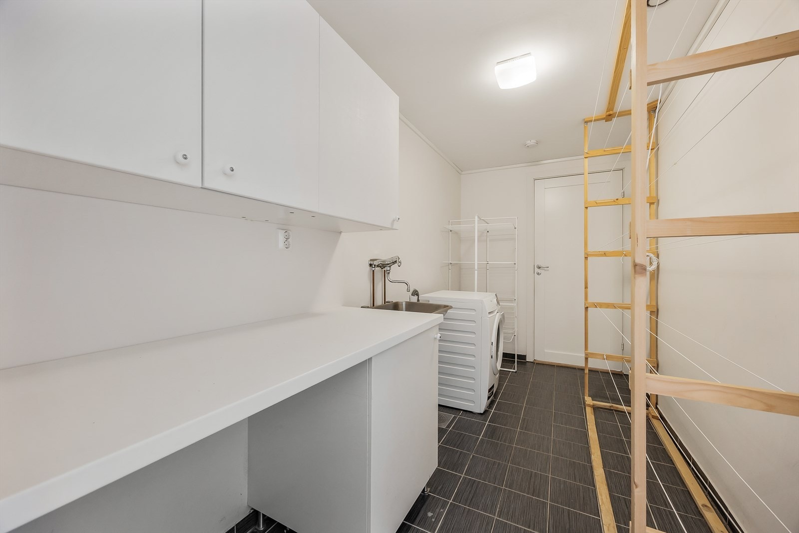 Et separat vaskerom med flislagt gulv, varmekabler og opplegg for vaskemaskin. Galleribilde