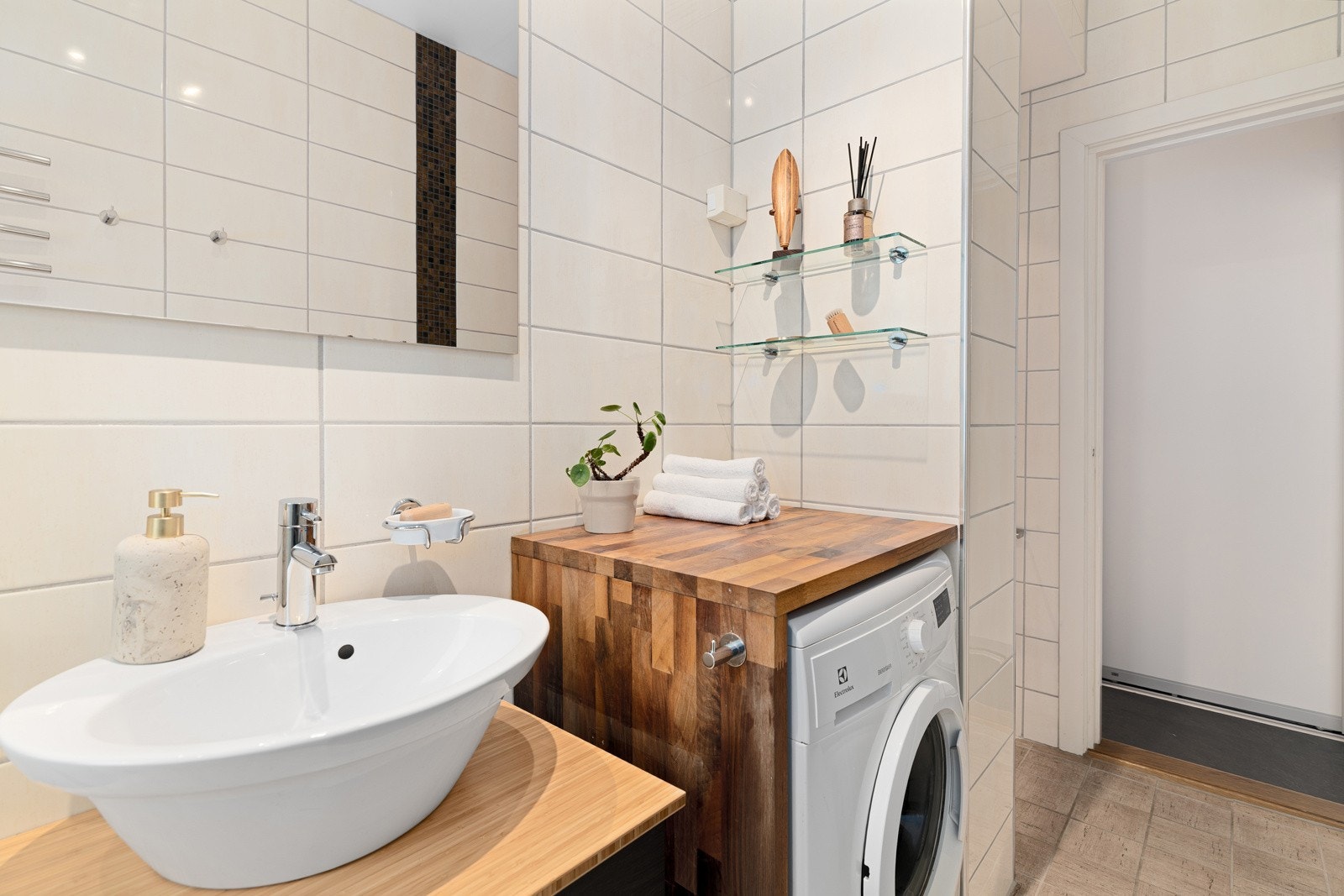 Badet er innredet med servantskap med skuffer, servant, speil, benkeplate med opplegg for vaskemaskin under, dusjkabinett og gulvstående toalett. Galleribilde