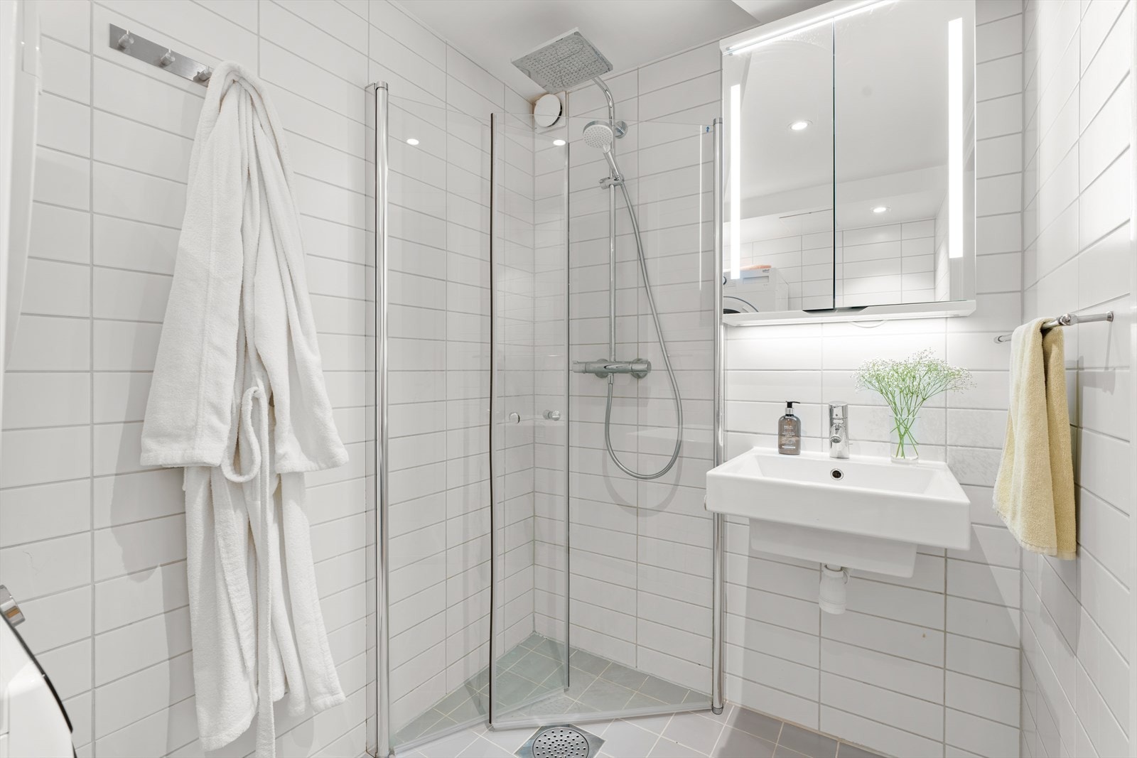 Badet er innredet med vegghengt klosett, servant, speilskap med lys og dusjhjørne med svingbare glassdører. Galleribilde