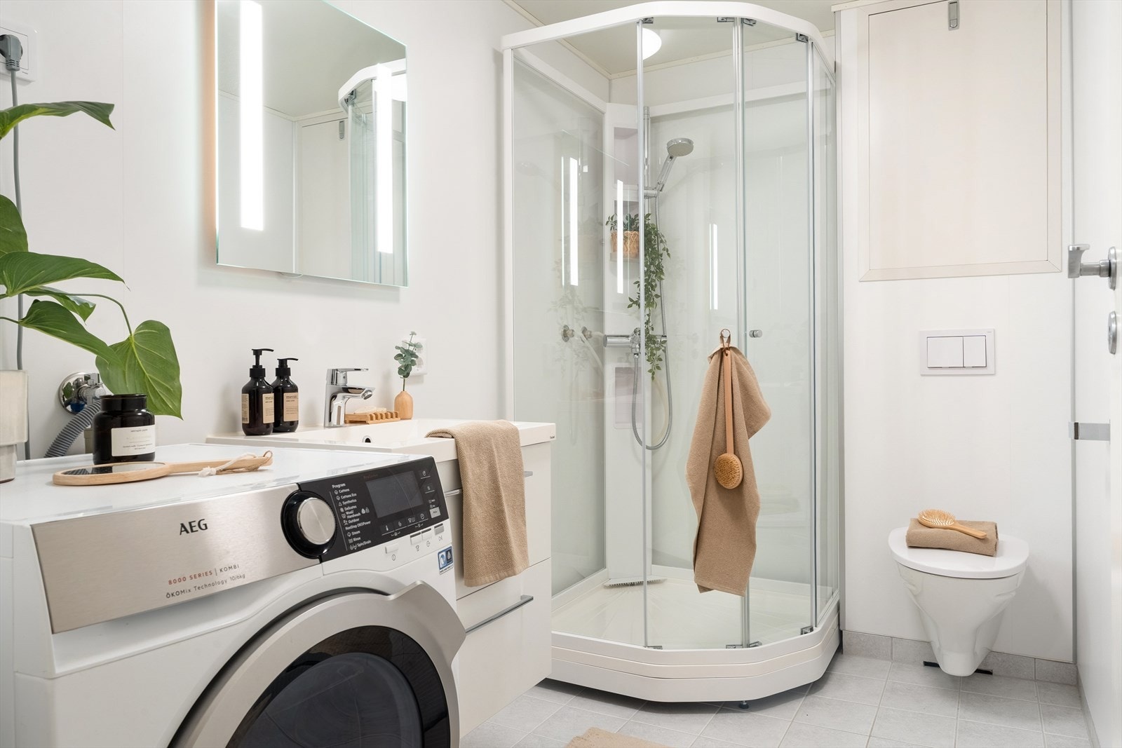 Badet er utstyrt med vegghengt toalett, helstøpt servant, skuffer under servanten med slette fronter, dusjkabinett og opplegg for vaskemaskin Galleribilde