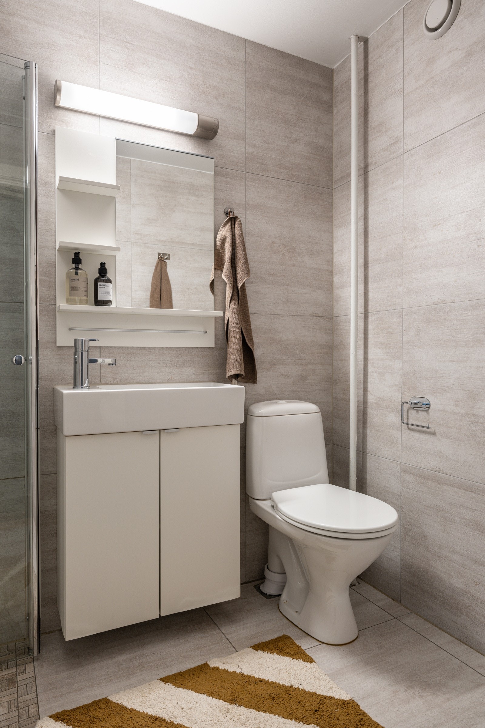 Lys baderomsinnredning med ovenpåliggende servant, speil med hyller og belysning over. Galleribilde