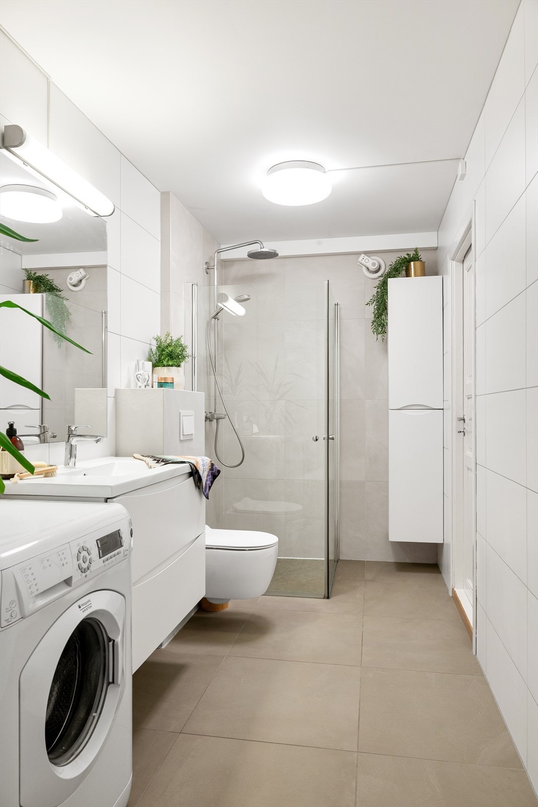 Romslig bad med stilrene fliser, servant med underskap, vegghengt toalett og praktisk dusjløsning. Galleribilde