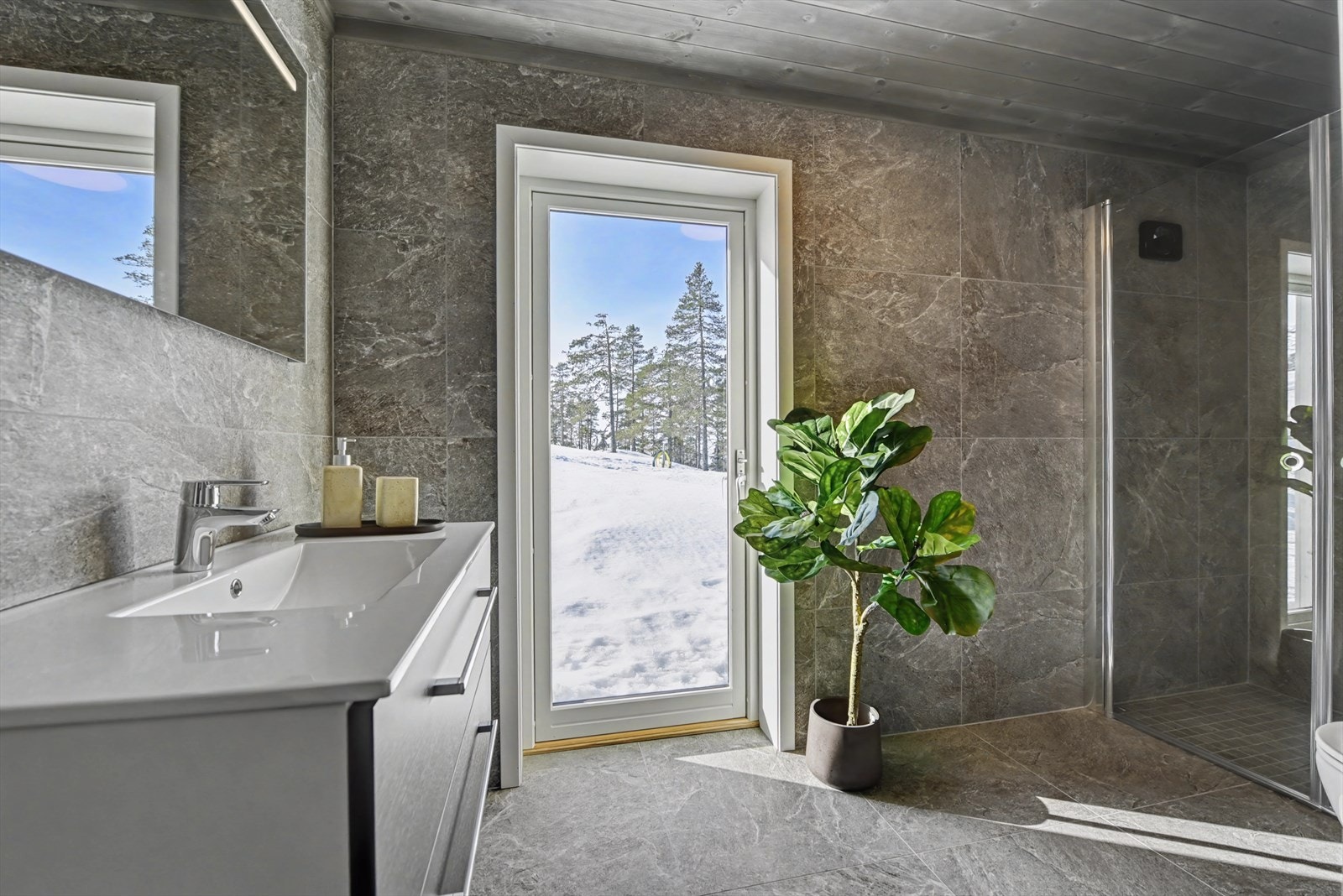 Badet i hytta er delikat med 60 cm x 60 cm fliser på gulv og vegg. Mørke fliser som gir et moderne utrykk. I dusjen er det nedsenk og 5 cm x 5 cm fliser. Galleribilde
