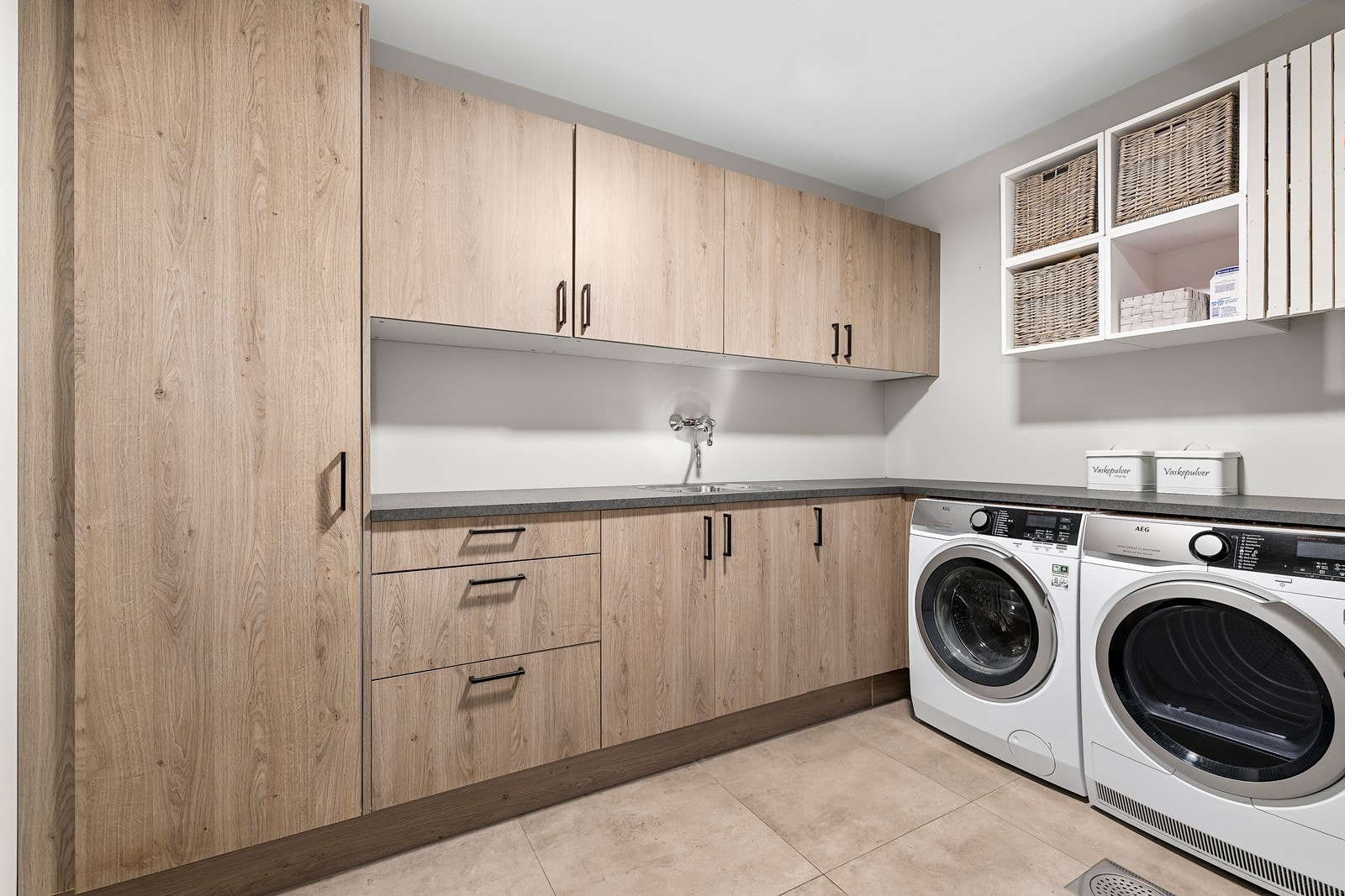 Vaskerommet har god oppbevaringsplass med gjennomgående romslig innredning og benkeflater. Det er plass til både vaskemaskin og tørketrommel side om side, samt åpne hyller for enkel organisering. Galleribilde